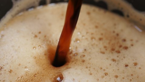 Dark beer is poured into a glass and beer foam is formed - shot in slow motion in extreme close up macro