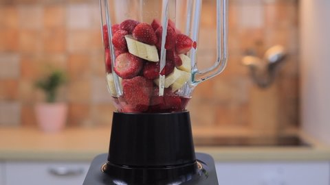 Blender with banana and strawberries making smoothie, close-up video