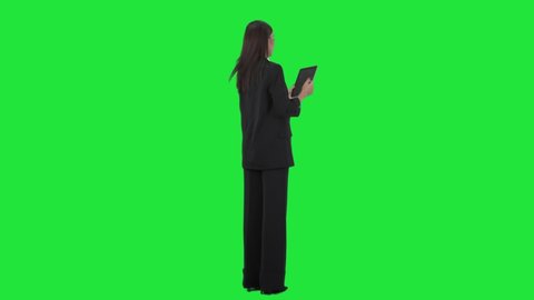 Back over the shoulder view of working business woman using tablet pad computer. Full length on green screen background.