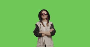 Young pretty girl wearing jacket hoodie chewing bubble gum over green screen background, Woman in sunglasses having fun on chroma Key . 4k raw video footage slow motion 60 fps