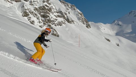 4K skiing footage, one woman skilled skier skiing on ski slope in long turns carving on sunny winter vacation day during ski holidays with clear blue sky high up in european alps mountains
