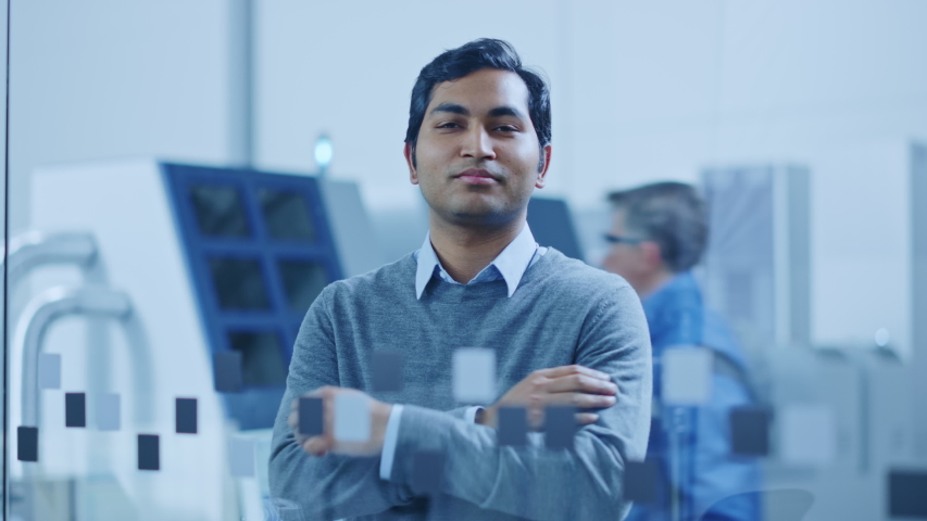 Modern Factory Office: Portrait of Handsome Indian Engineer Crosses Arms and Smiles Charmingly. In the Background High Tech Facility with CNC Machinery, Robot Arm and People Working Royalty-Free Stock Footage #1046400682