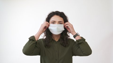 Young woman takes off medical mask. Female breathes deeply and smiling looking at camera. Isolated on white  background. Health care and medical concept. Close up portrait . 4k