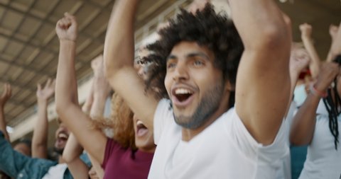 Young couple watching a sport event, jumping with hands raised, giving each other high five and hugging. Excited crowd of sports fans applauding and celebrating their team's victory. 