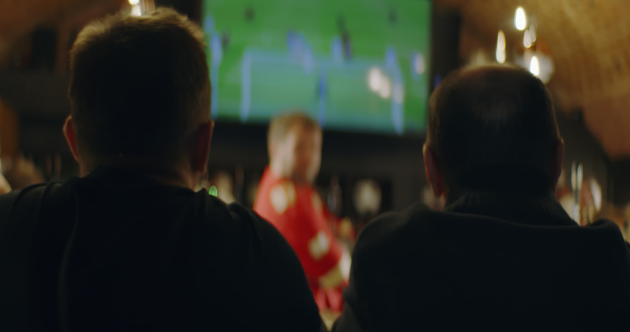 HANDHELD Model released, fans watching a game on a large TV in a sport pub. Shot on ARRI Alexa Mini with Atlas Orion 2x Anamorphic lens | Shutterstock HD Video #1046417368