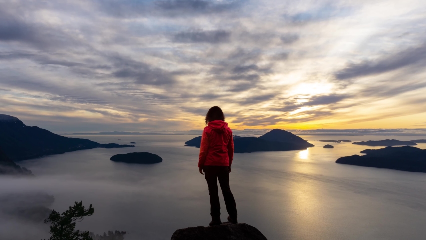 Time Lapse. Adventure Female Hiker on top of a high rocky mountain peak during a vibrant winter sunset. Composite Image Animation. Taken in Howe Sound near Vancouver, British Columbia, Canada. Royalty-Free Stock Footage #1046420944
