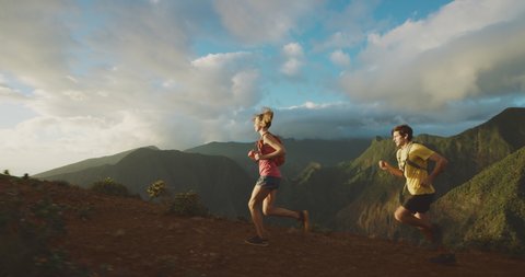 Young athletic man and woman running together outdoors on a mountain top at sunset, two friends exploring the mountains together, weekend summer adventures