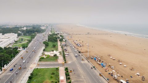 Wide shot of time lapse of marina beach and vehicles moving on busy straight road during rush hour next to the Bay of Bengal, Chennai, India