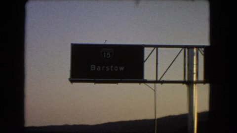 NEVADA USA-1966: Driving Past And Old Town And A Freeway Sign For Barstow Freeway
