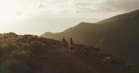 Aerial view of two runners exploring a mountain ridge top at sunset, young adventurous couple running on an amazing trail in the mountains