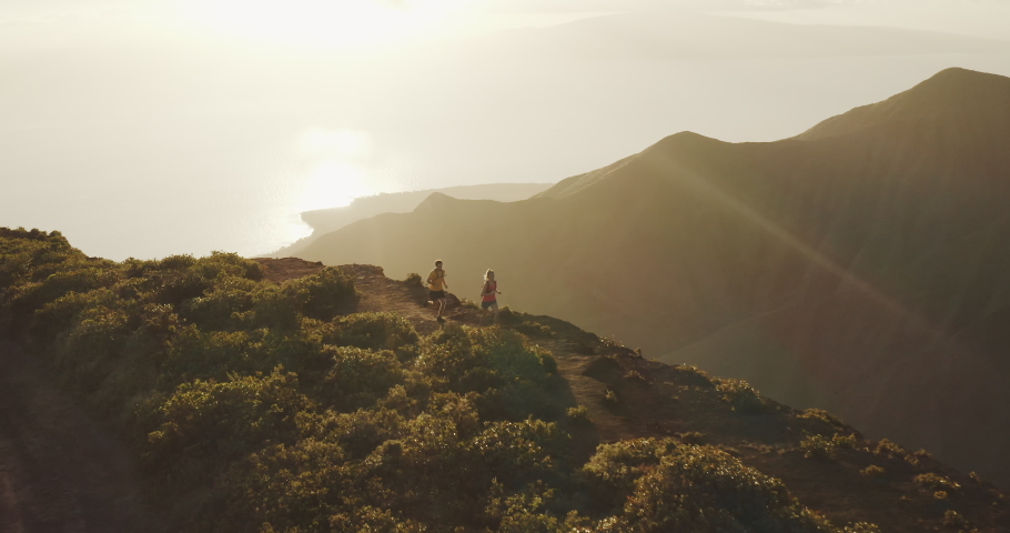 Aerial view of two runners exploring a mountain ridge top at sunset, young adventurous couple running on an amazing trail in the mountains