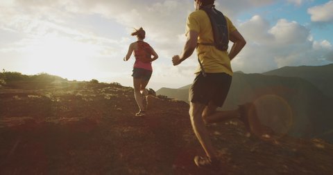 Two young active friends running outdoors together on a mountain top at sunset, adventurous couple exploring new places together