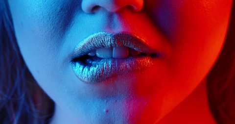 Sensual girl with bright glowing lipstick seductively biting her lips in neon light - nightlife, nightclub concept extreme close up shot 4k footage