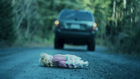 Creepy and eerie shot of car driving off leaving doll behind on ground