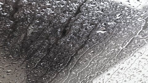 rain falls heavily on the window forming many drops while camera zooming in