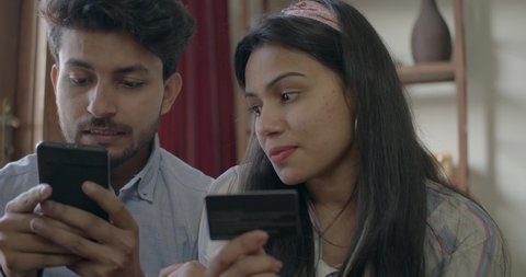Indian couple discuss and buy online together as they share their smart phone mobile phone using their bank debit cards and celebrate with high five their hands, slow-motion handheld 60 fps