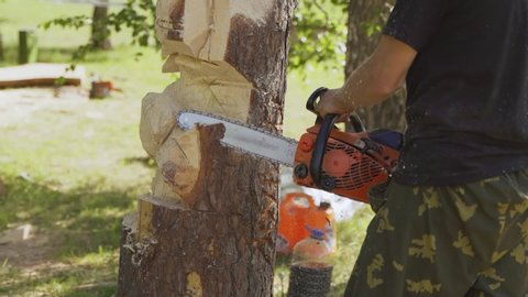 A man carves a wooden statue from a log with a chainsaw. Wooden sculptures.