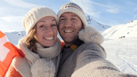 Young couple take selfies holding Swiss flag in the airs with snowy mountain peaks in the background 