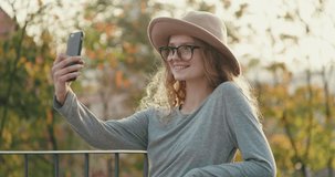 Attractive woman standing by the Fence on Terrace and making Selfie on her Mobile Phone. Looking stylish and Gorgeous. Casually dressed Young Girl Enjoying Lifestyle Outdoor. Having charming smile.