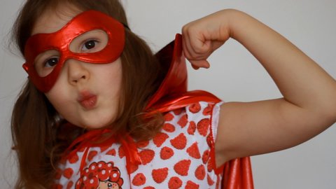 Cute baby girl plays superhero. Funny child in a red raincoat and mask playing power super hero. Superhero and power concept. Portrait close up