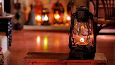 A man puts a lighted  kerosene lamp on a table, on a shelf. lanterns are lit in the background