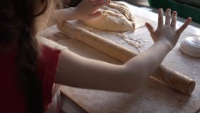 Little Caucasian girl rolls out the dough using a wooden rolling pin. Handmade homemade cakes. 4K video.