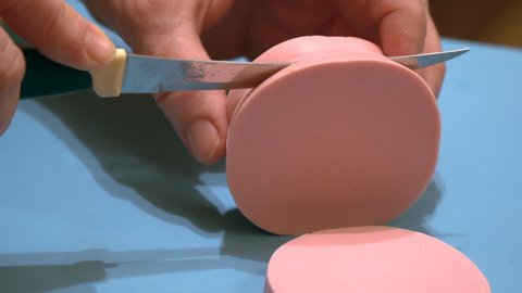 A woman cuts a pink delicious cooked sausage into pieces with a knife