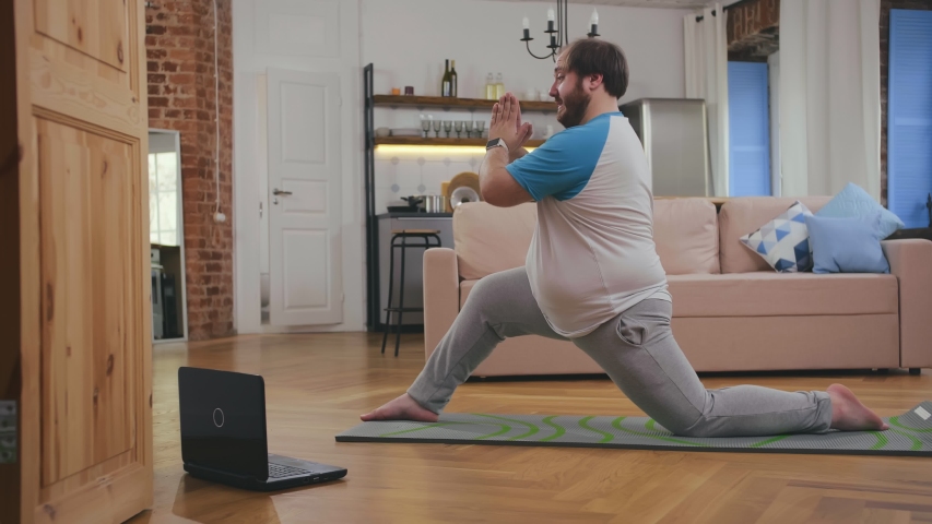 fat man doing gymnastics for losing weight at home on mat on floor watching tutorial video on laptop. Overweight guy doing yoga exercises at home. Royalty-Free Stock Footage #1046488777