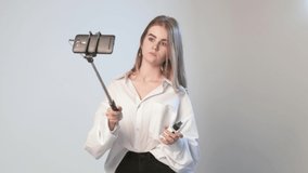 young female records video with smartphone attached to selfie stick. blond girl filming tutorial vlog about eyebrows cosmetics and makeup, using cellphone isolated on white background. Beauty blogger
