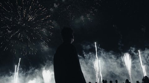 The guy looks at the Beautiful fireworks in the night sky. Pyrotechnic performance fireworks, firecrackers, fires and explosions.Holiday Festival Event.And he smilesGolden shining with bokeh 4K.