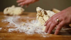 Slow motion clip of female hands kneading pie dough on floured surface.