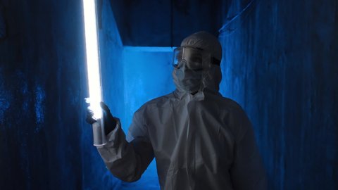 Hazmat suit wearing woman explores a dark tunnel. Female in protective suit, mask and glasses with flashlight walking in dark tunnel, looks around.