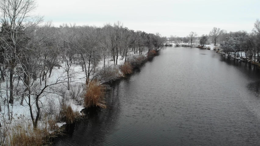 Beautiful view from the drone along the river to shore and snowy winter forest.