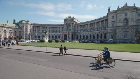VIENNA AUSTRIA July 06 2019 Vienna City Bikes - moving shot of a young couple riding on two free city bicycles on the Heldenplatz, background tourists and the Hofburg Palace, with sound