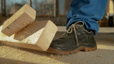 SLOW MOTION, CLOSE UP, DOF: Detailed shot of a painful work accident as a heavy plank falls on an unrecognizable worker's foot. Worker sawing wood drops a beam on his foot. Construction site accident