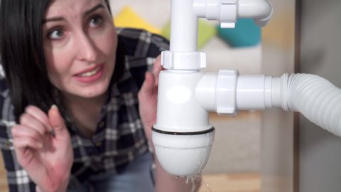 Young woman in a shirt discovered a leak under the sink and calls the plumber