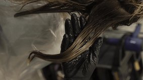 Girl at the hairdresser in the salon applied with paint, lotion, oil, cream on her hair smearing them with her hand in black gloves and holding brush in her hands vertical orientation video frame 9:16