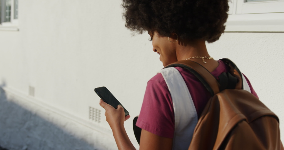 Over the shoulder view of mixed race woman enjoying free time on a street on a sunny day, walking, using the phone, slow motion, slow motion | Shutterstock HD Video #1046549296