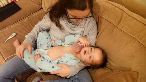 A mother cradles her toddler girl who is sick with RSV and has a fever and oxygen tubes up her nose to help her breathe