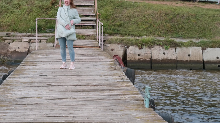 Woman in blue coat and pink sport shoes laughs and runs ahead towards camera.