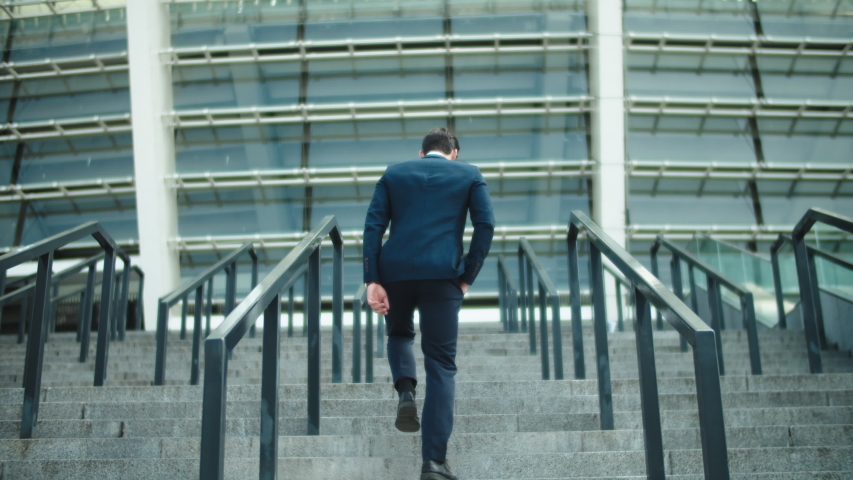 Back view stylish business man going upstairs in suit at street. Successful businessman walking at stairs alone outdoors. Young man walking in luxury suit near stadium. Royalty-Free Stock Footage #1046562637