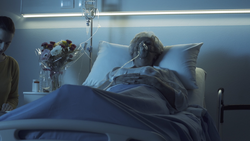 Young woman assisting her sick mother sleeping in a hospital bed with oxygen mask, senior care concept | Shutterstock HD Video #1046569453