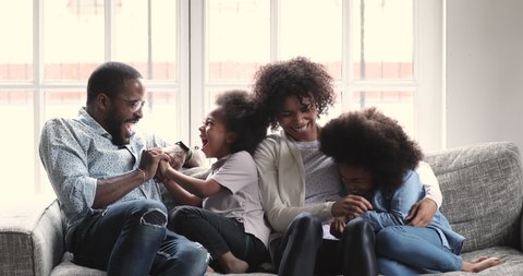 Cheerful affectionate afro american family having fun relaxing on sofa, happy african adult parents tickling laughing cuddling at home playing lifestyle game bonding enjoying funny moments at home
