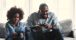 Happy young dad and cute child kid daughter gamers winners holding controllers playing winning video game give high five sit on sofa celebrating victory enjoying leisure activity at home