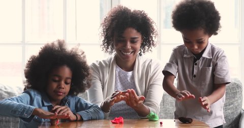 Afro american family young adult mom teacher nanny teaching two cute little african kids learning playing together sculpting playdough toys on table enjoying creative leisure activity concept at home