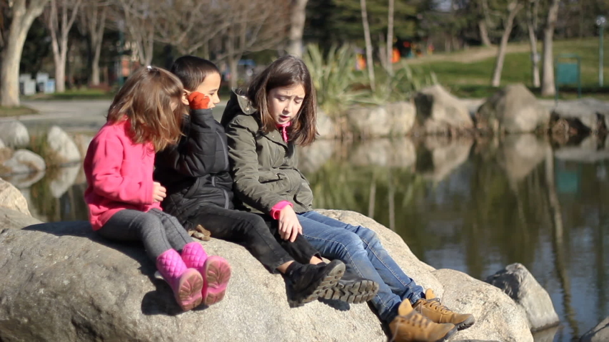 Three kids playing in the nature. Children throw stones at the lake shore. Sunny autumn day
