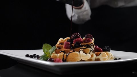 Chocolate sauce pouring on belgian waffles. Sweet breakfast food, unhealthy eating. Sugar food. Pouring syrup over waffles on plate with berries and ice-cream. Slow motion. Full hd