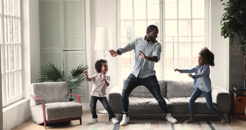 Happy active african american dad teaching dancing having fun with two cute small kids son and daughter imitate father moves playing together enjoying funny weekend activity in modern living room