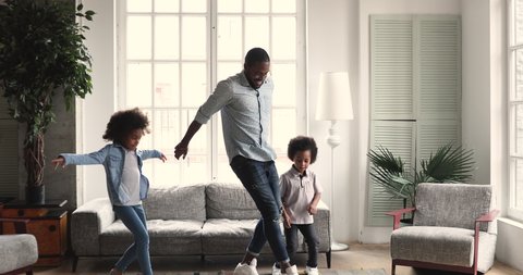 Funny afro american little children preschoolers dance copy young adult father in living room interior, happy african family dad babysitter and two active energetic kids having fun at home together