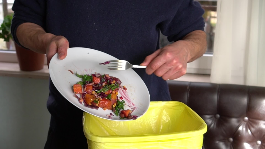 Food waste or food loss. A man throws the uneaten meal from a plate in the trash bin. Throwing away holiday dinner | Shutterstock HD Video #1046577757